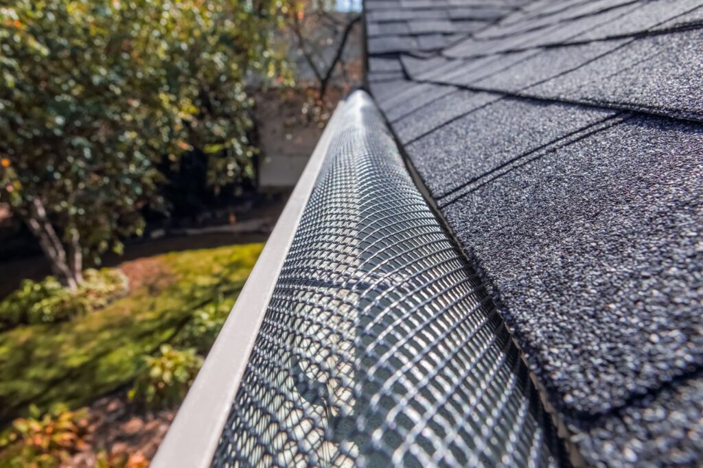 A gutter with a metal mesh guard on a house with a gray shingle roof.