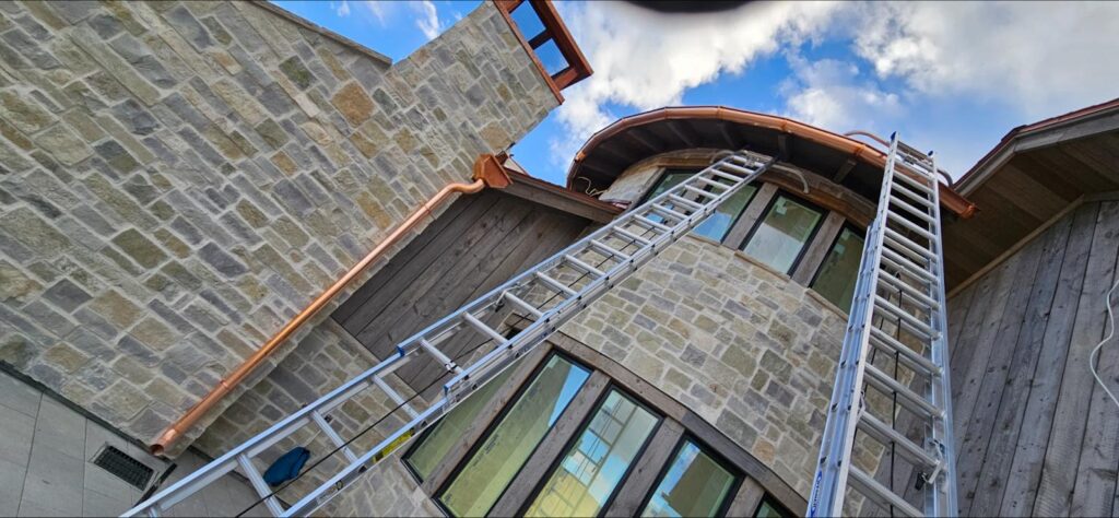 Ladders against a stone house with a copper gutter.