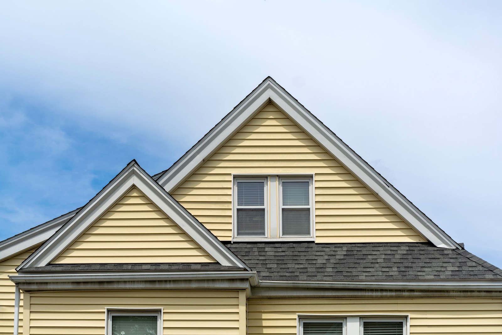 Top view of a yellow house with a dark roof under a clear blue sky.
