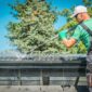 A man in overalls and gloves is cleaning a roof using a brush to remove debris under a clear blue sky 85x85
