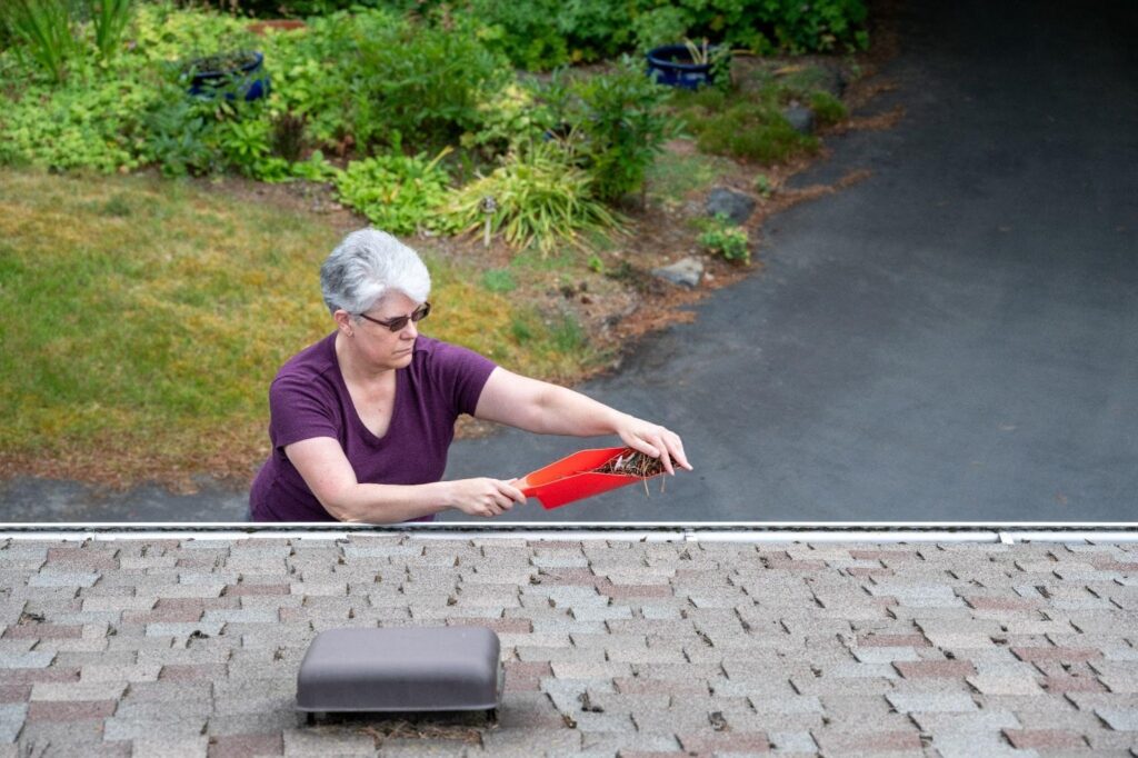 A woman sweeping the roof of a house with a broom focused on cleaning debris from the surface