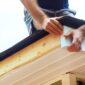 A man works on a roof installing a new gutter with tools in hand and a focused expression on his face 85x85